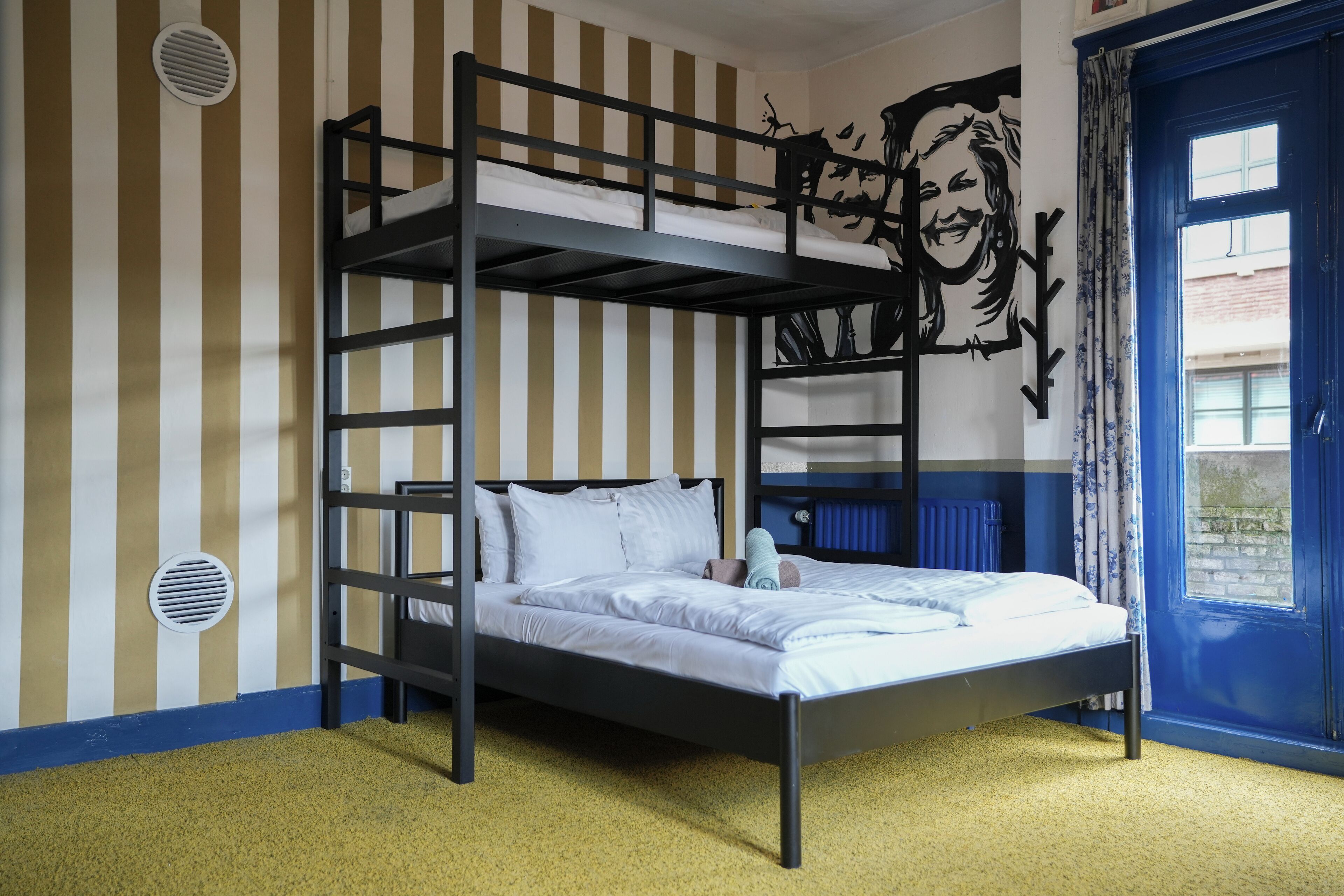 A bunk bed room with a striped wall, a mural, and a window with blue curtains.