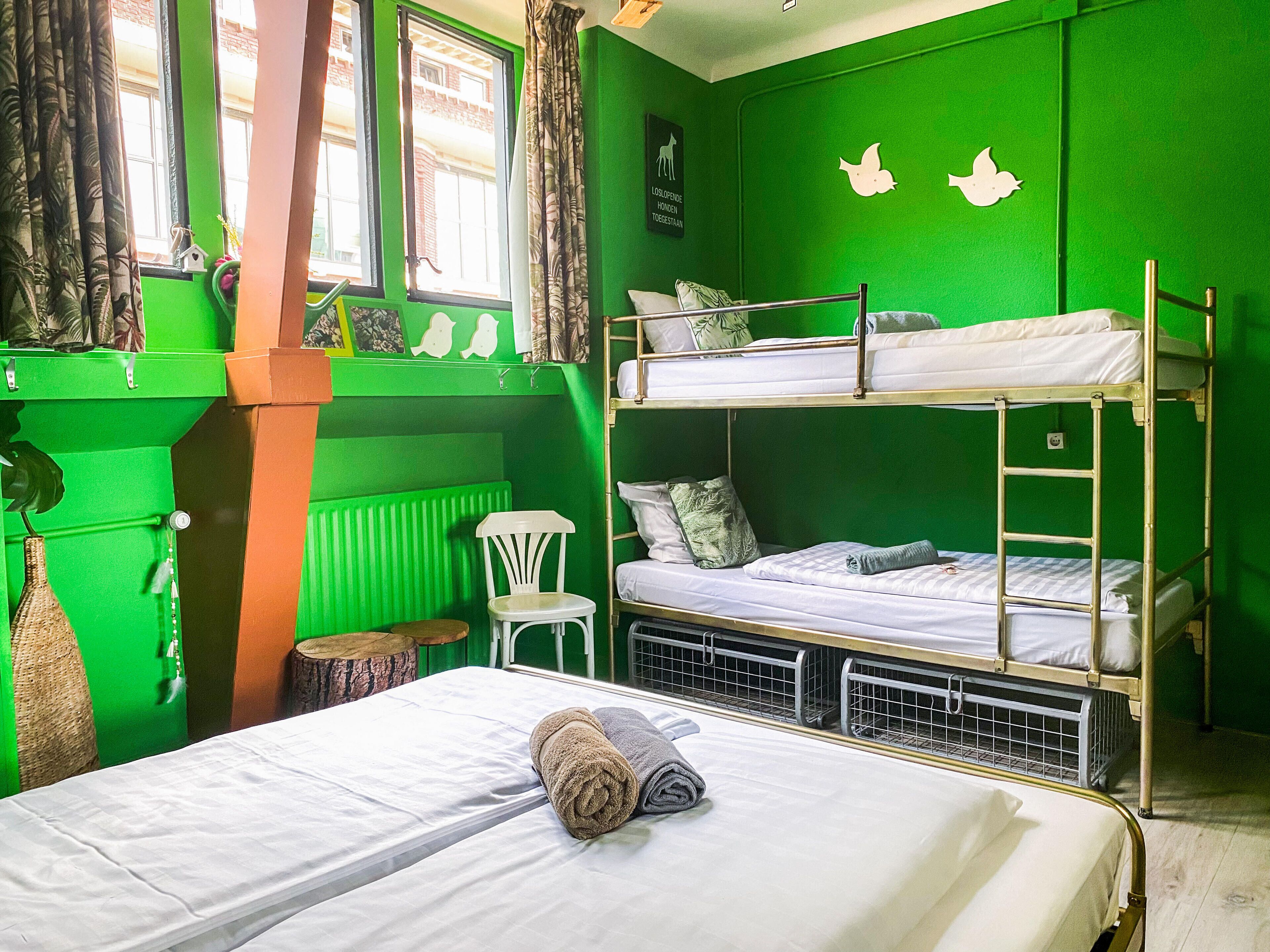 Ein Schlafzimmer mit Etagenbetten, grünen Wänden, einem kleinen weißen Stuhl und einem Fenster mit Vorhängen.