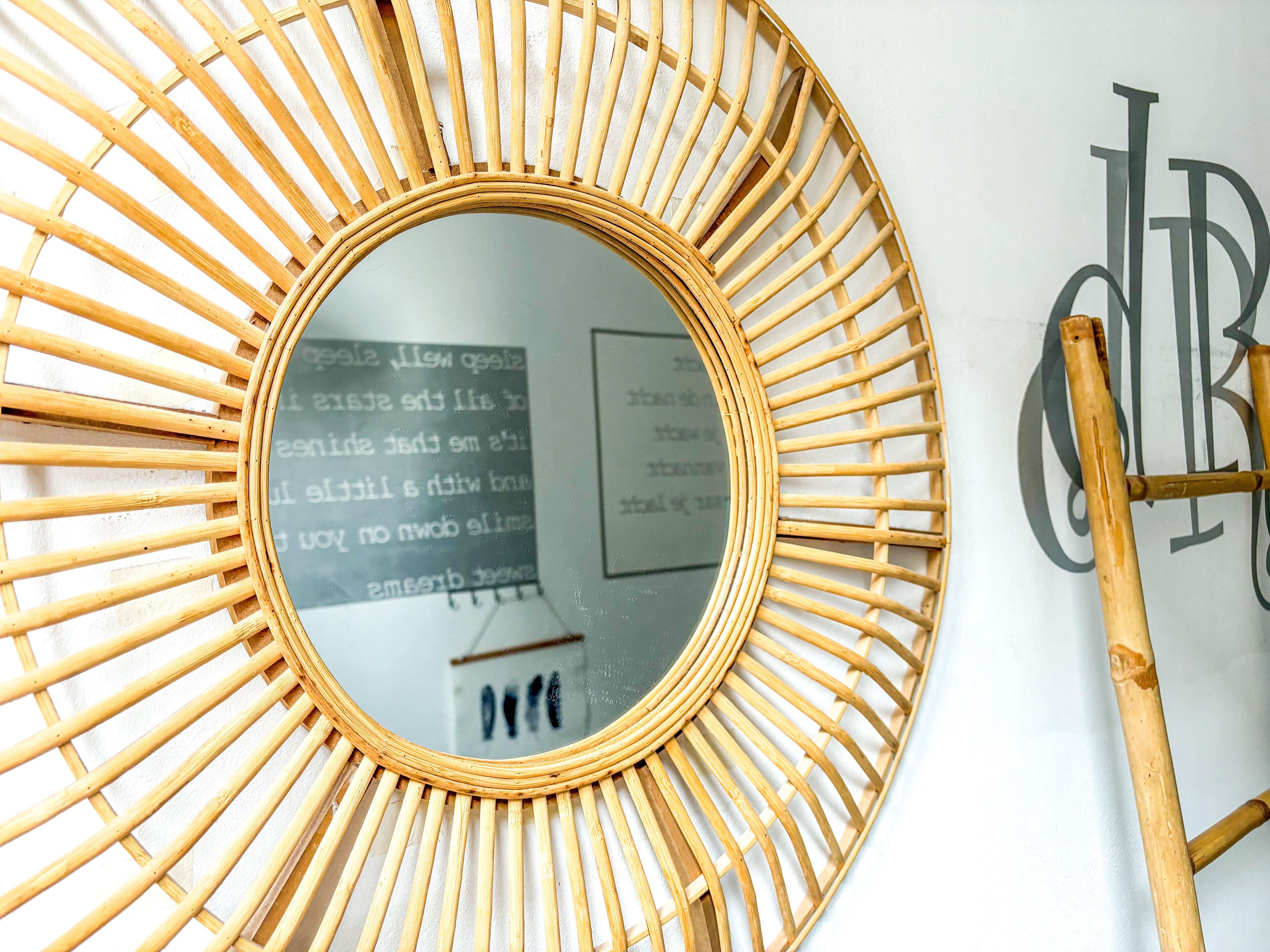 A circular mirror with a bamboo frame, mounted on a wall with a partial view of a letter 'B' and a wooden ladder leaning against the wall.