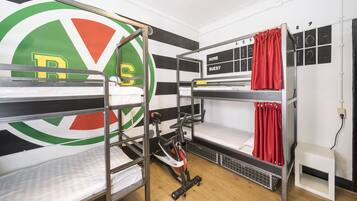 A dormitory room with bunk beds, a bicycle, a chalkboard with room numbers, and a window with curtains.