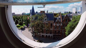 A view through a circular window of a cityscape with historic buildings, a church spire, and modern high-rises. - Hostel ROOM Rotterdam (Rotterdam)