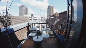 A rooftop terrace with a wooden deck, white metal chairs, a round table, and a potted plant. - Hostel ROOM Rotterdam (Rotterdam)