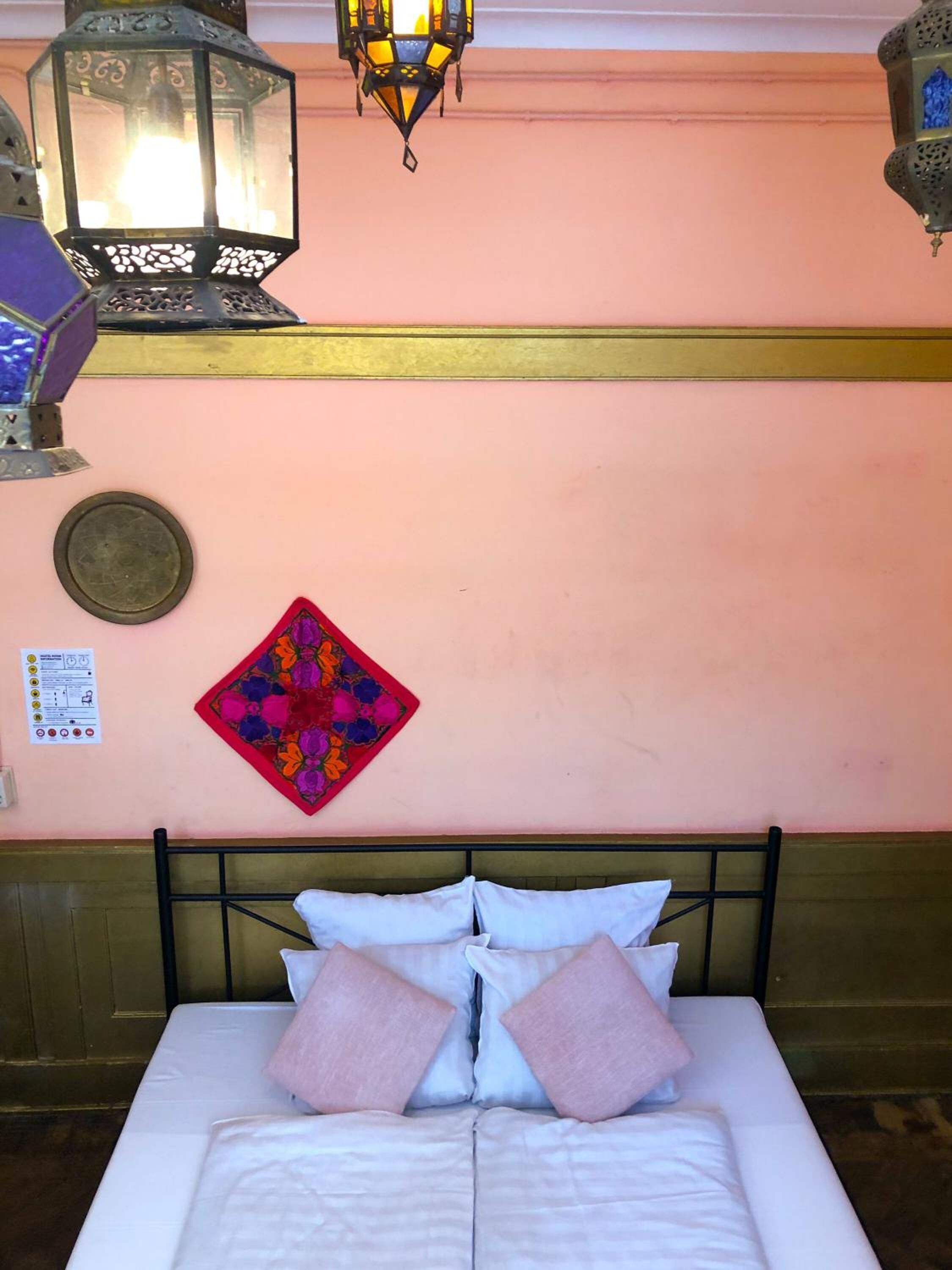 Ein Bett mit weißer Bettwäsche und zwei rosafarbenen Kissen, ein dekoratives Wandbild sowie zwei aufwändige Wandleuchten.