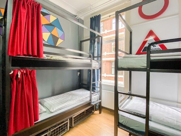 A dormitory room with bunk beds, a geometric wall decoration, and a view of a building through a window. - Hostel ROOM Rotterdam (Rotterdam)