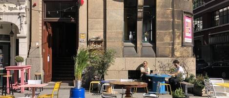 An outdoor seating area with tables and chairs, a blue barrel, and a person sitting at a table.