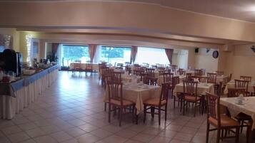 A spacious dining area with multiple tables and chairs, large windows allowing natural light, and a bar area with a counter and seating.