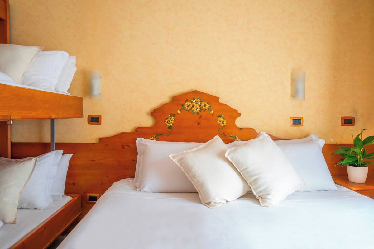 Une chambre d’hôtel avec un lit superposé en bois, un lit simple avec une literie blanche et une plante en pot sur la table de chevet.