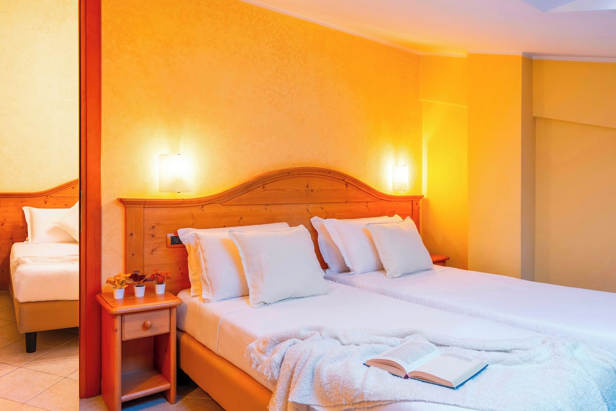 Une chambre d’hôtel avec une tête de lit en bois, un lit simple, une table de chevet avec une lampe et une petite table sur laquelle est posée une plante.