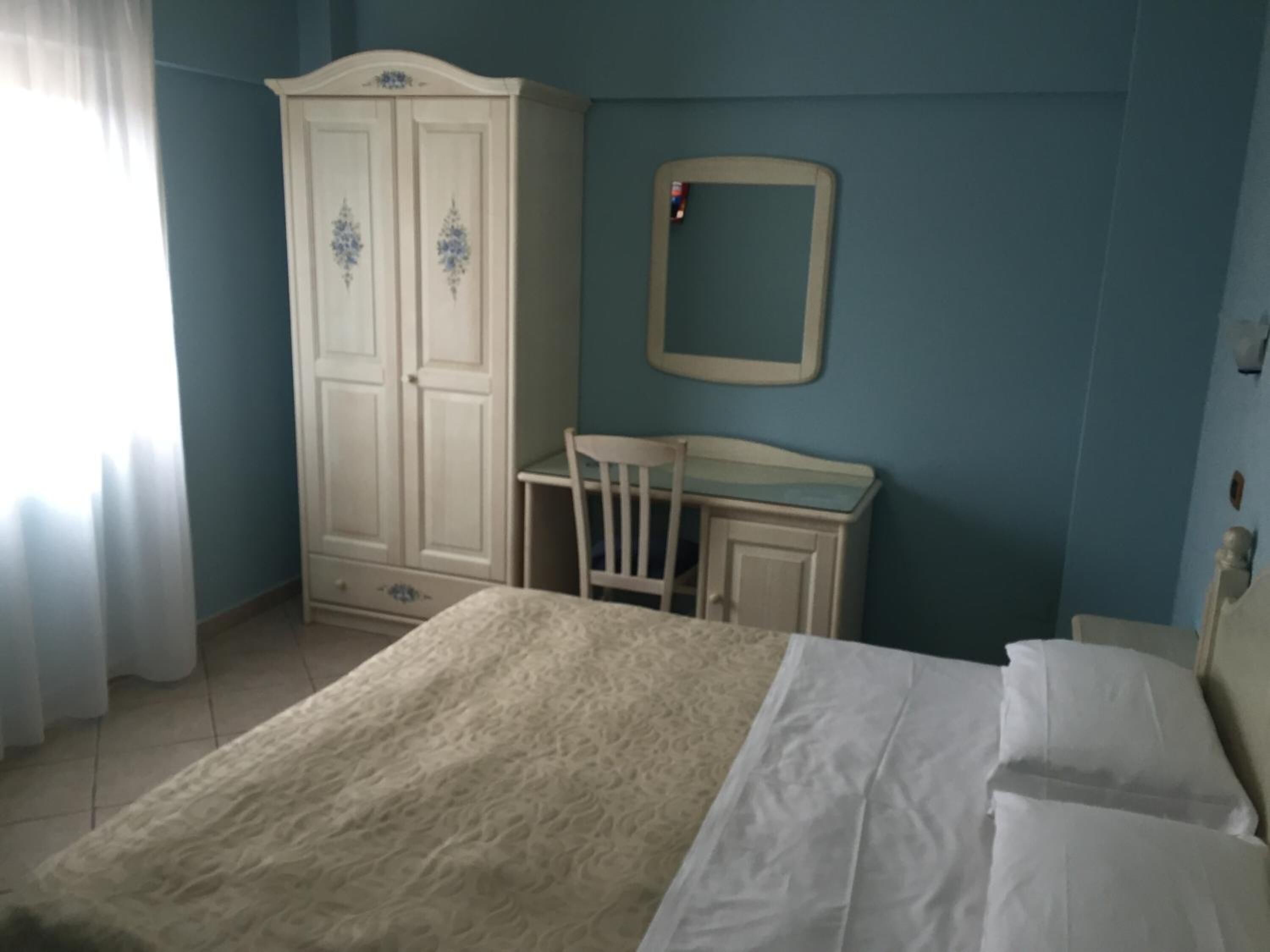 A bedroom with a bed, a desk, a chair, a wardrobe, and a mirror on the wall.