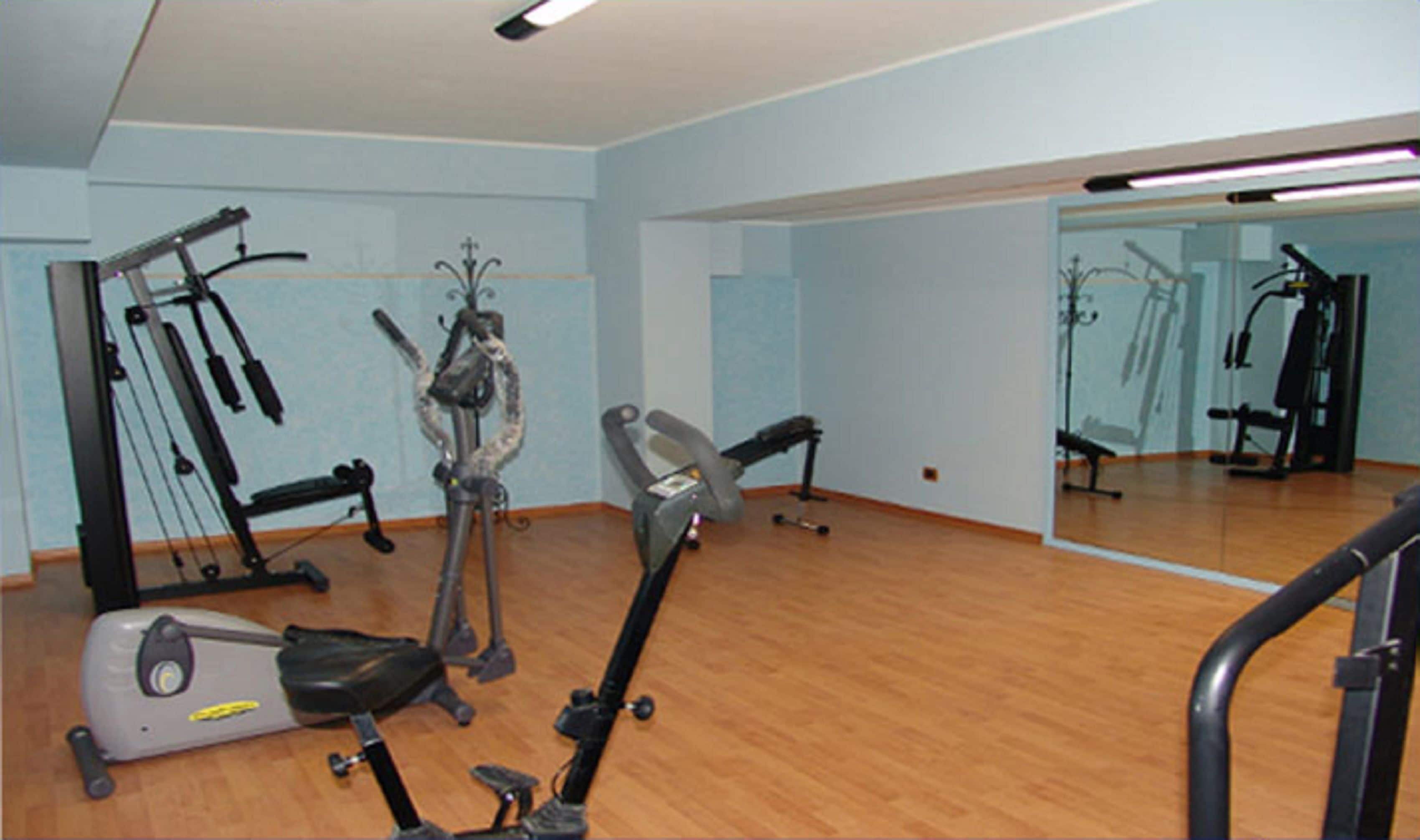 A gym with exercise equipment, a mirror, and wooden flooring.