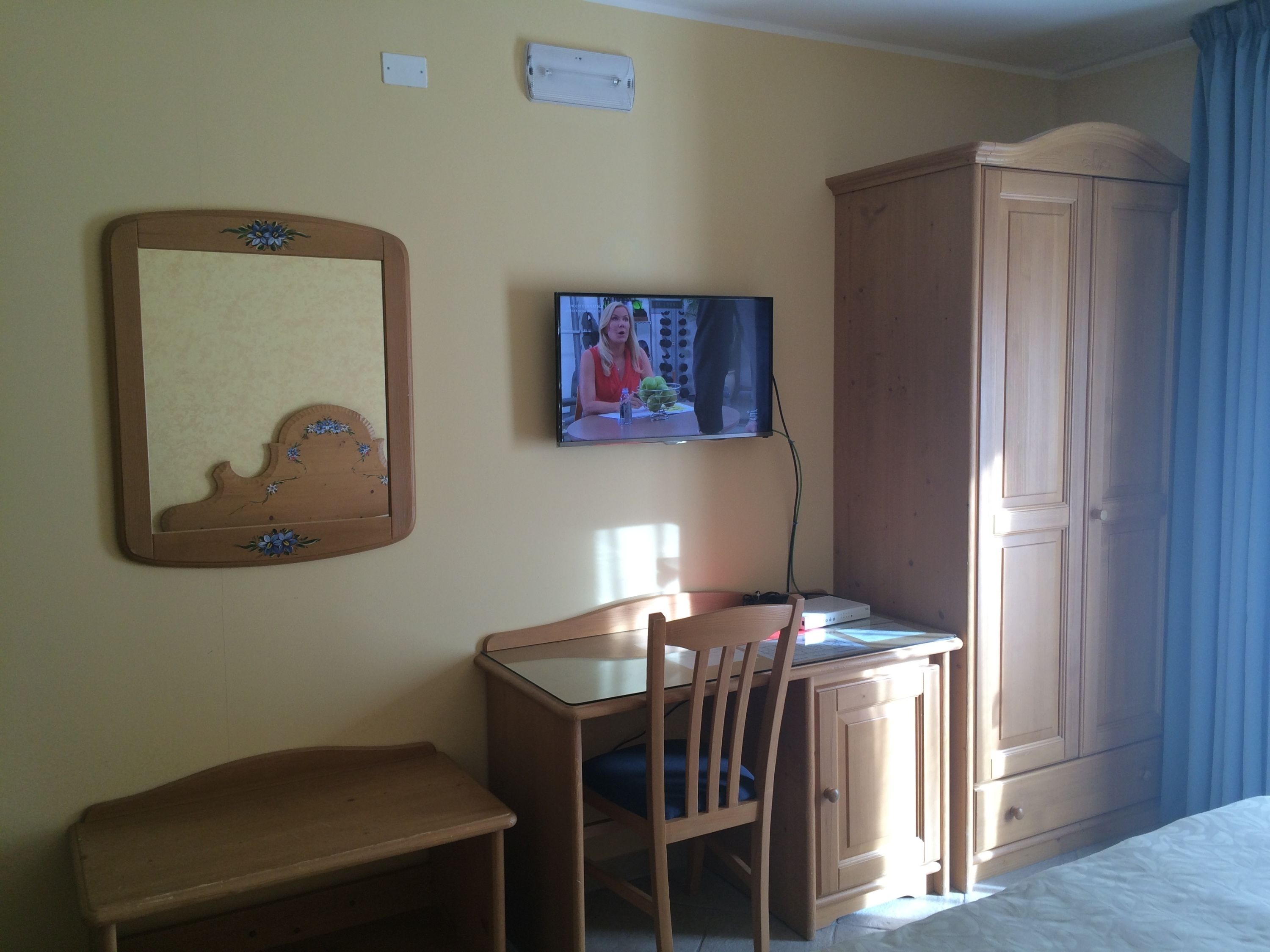 Una habitación de hotel con un escritorio de madera, una silla, un televisor, un armario y un espejo.
