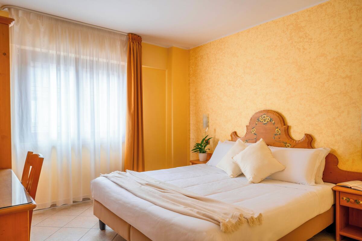 Une chambre d’hôtel avec un lit, une table de chevet, une plante en pot et une fenêtre avec des rideaux.