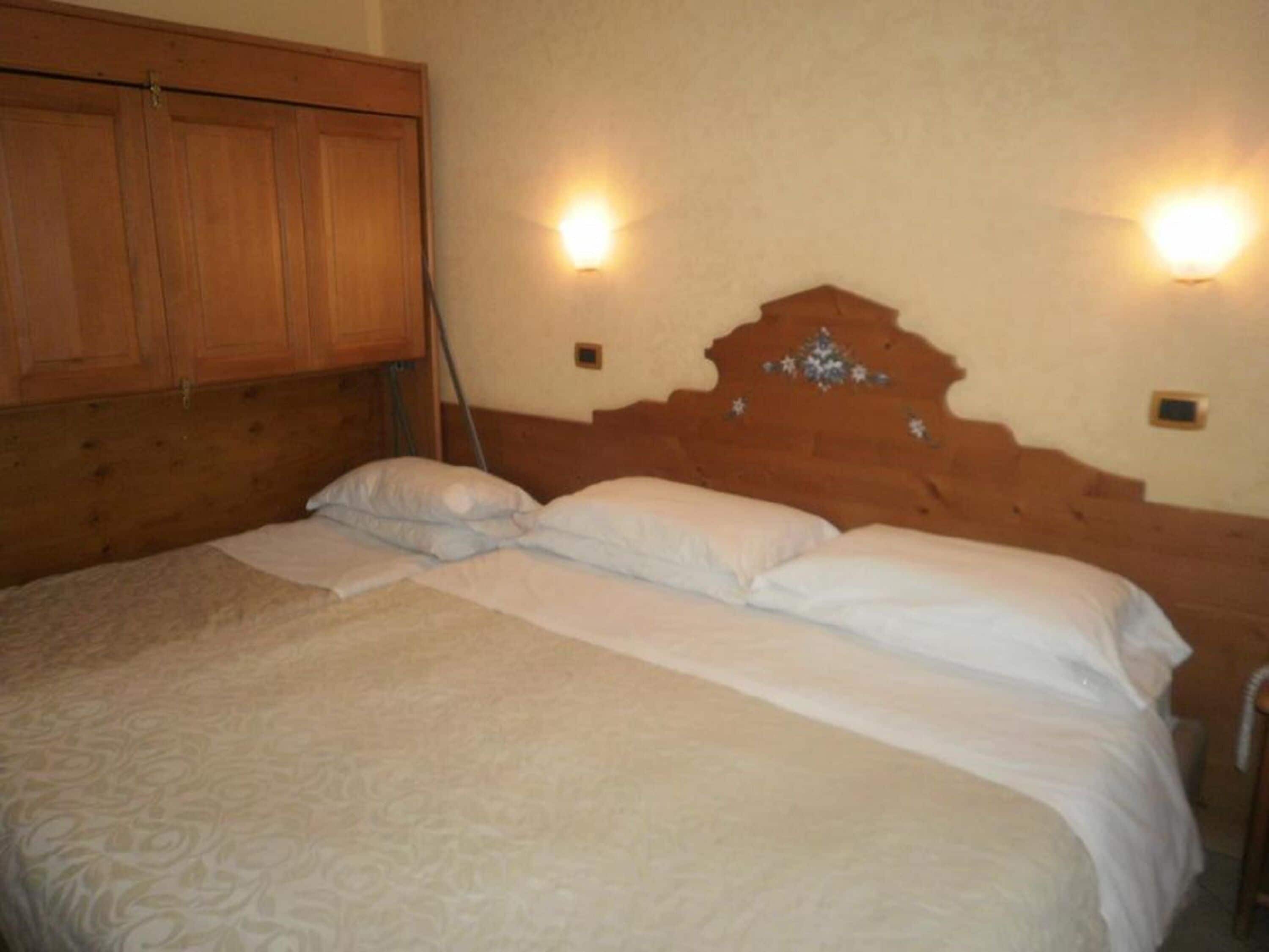 Un dormitorio con cabecera de madera, dos luces fijadas a la pared y cama con ropa blanca.