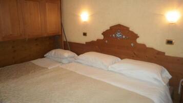 Un dormitorio con cabecera de madera, dos luces fijadas a la pared y cama con ropa blanca.