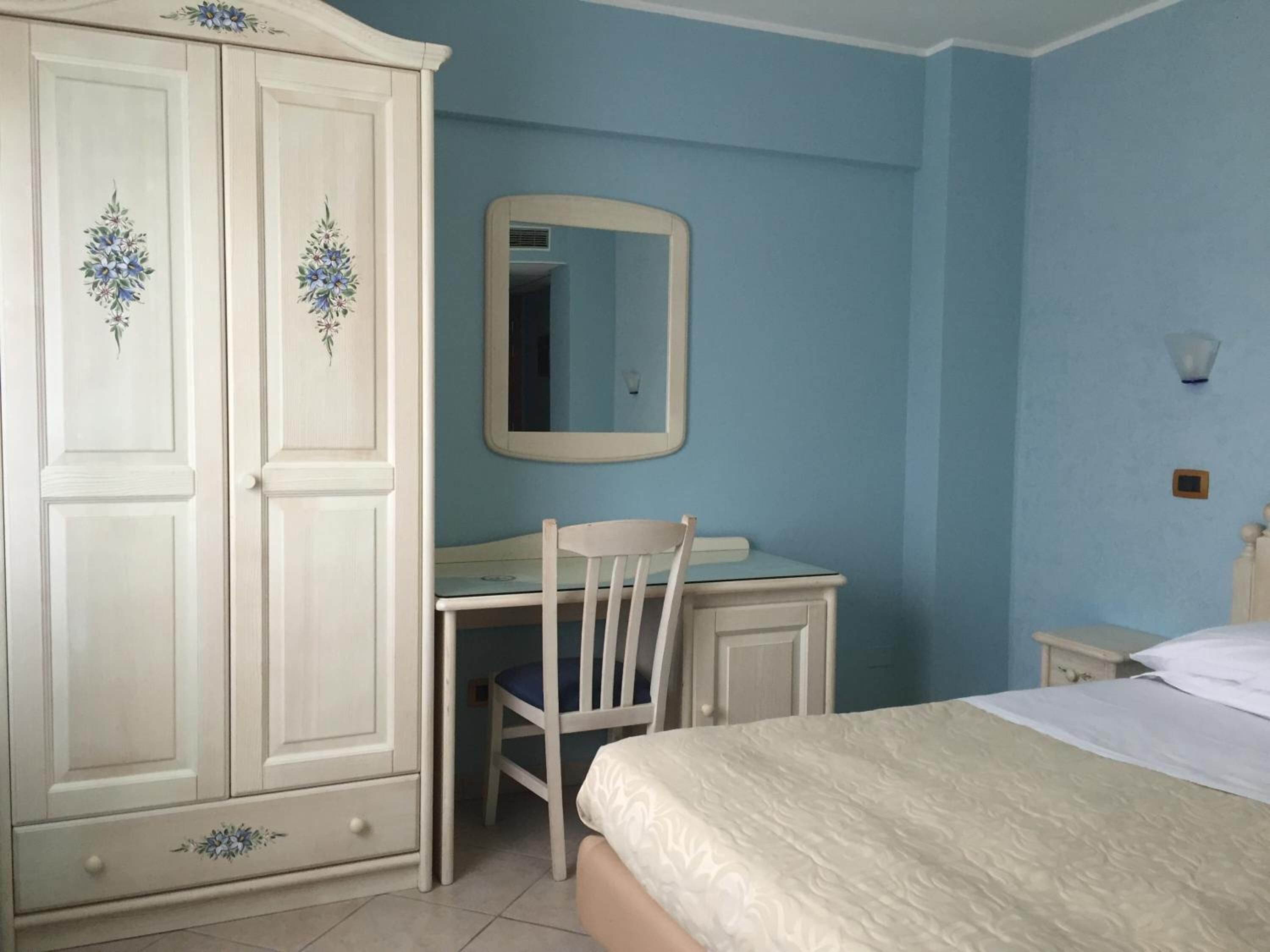Ein Schlafzimmer mit Bett, Schreibtisch, Stuhl, Kleiderschrank und Spiegel.