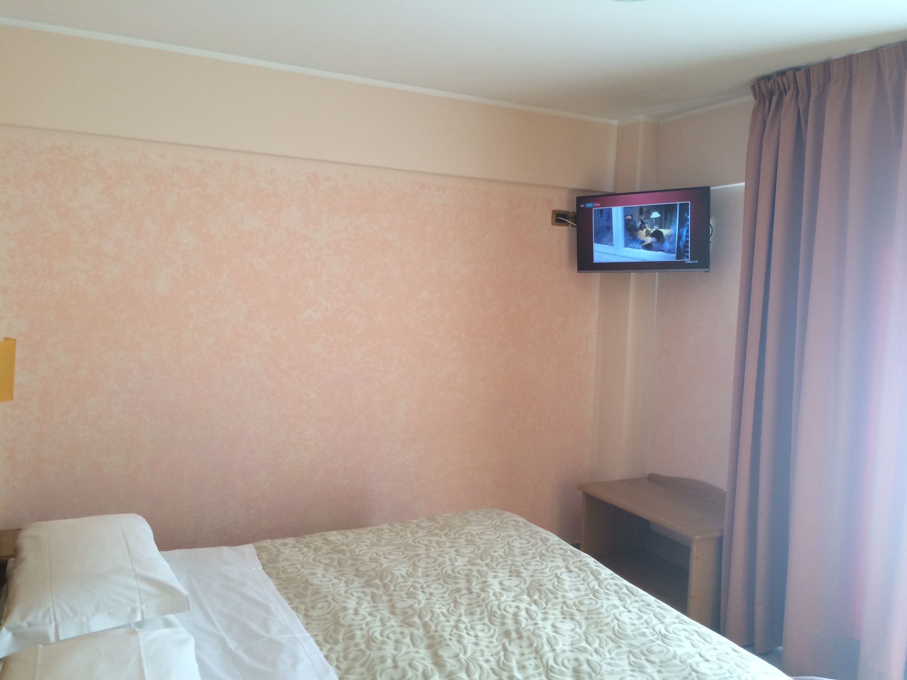 A hotel room with a bed, a television mounted on the wall, and a window with curtains.