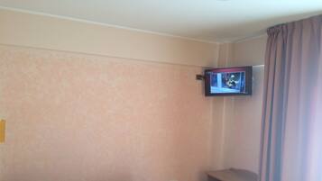 A hotel room with a bed, a television mounted on the wall, and a window with curtains.