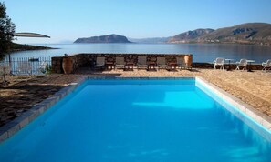 Una piscina con un muro de piedra y sillas, con vistas a un lago y montañas al fondo.