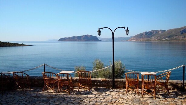 A seaside terrace with wicker chairs and tables, overlooking a calm lake with distant mountains. - Annema Hotel (Monemvasia)