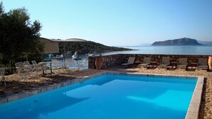 A pool with a stone wall and lounge chairs, overlooking a body of water and a distant island. - Annema Hotel (Monemvasia)