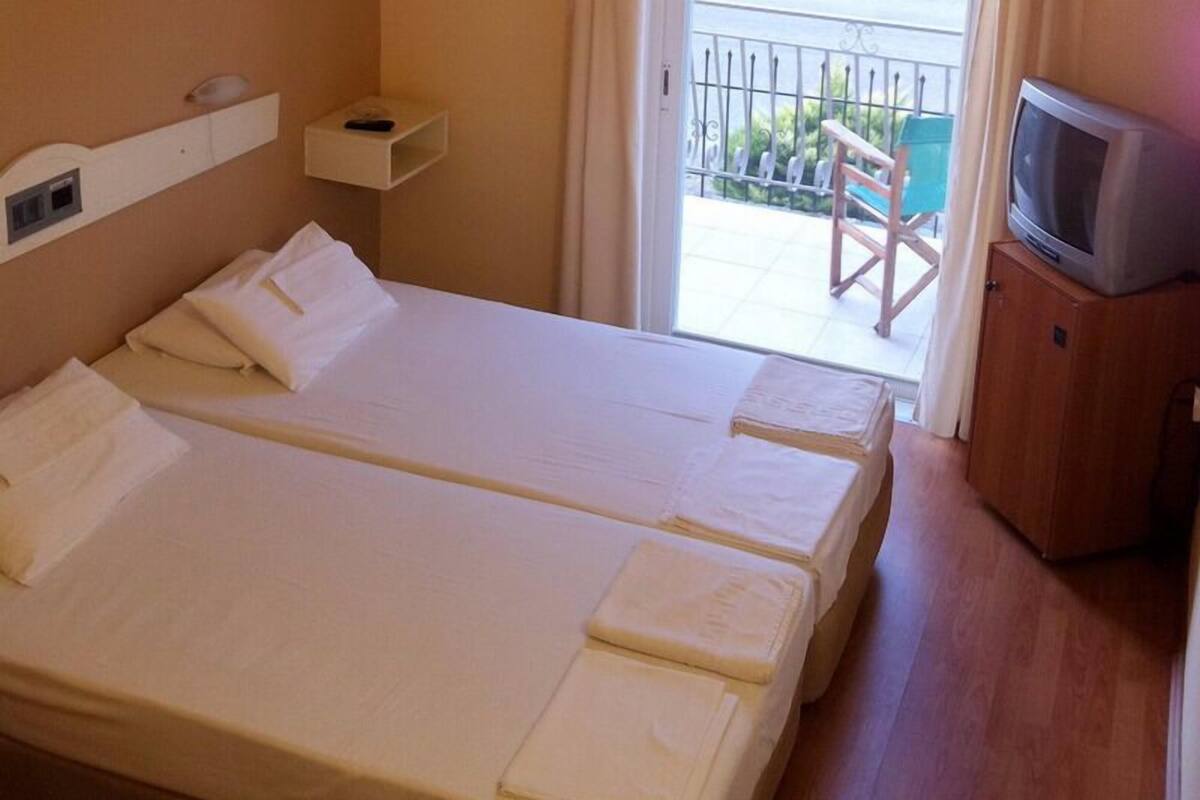 Habitación de hotel con dos camas, un televisor sobre un mueble y un balcón con sillas.
