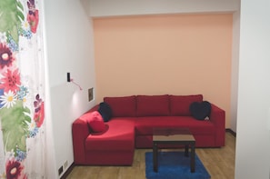 A red sectional sofa with a matching ottoman and a small table in a room with wooden flooring and a blue rug. - Arcobaleno Sanremo (Sanremo)