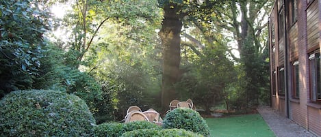 Un jardín con setos bien cuidados, césped y sillas de mimbre.