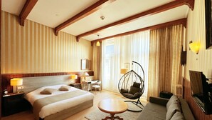 Una habitación de hotel con una cama grande, un sofá, un sillón colgante, un escritorio y un televisor.