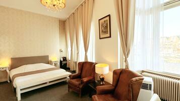 A hotel room with a bed, two leather armchairs, a table with a lamp, a picture on the wall, and a radiator.