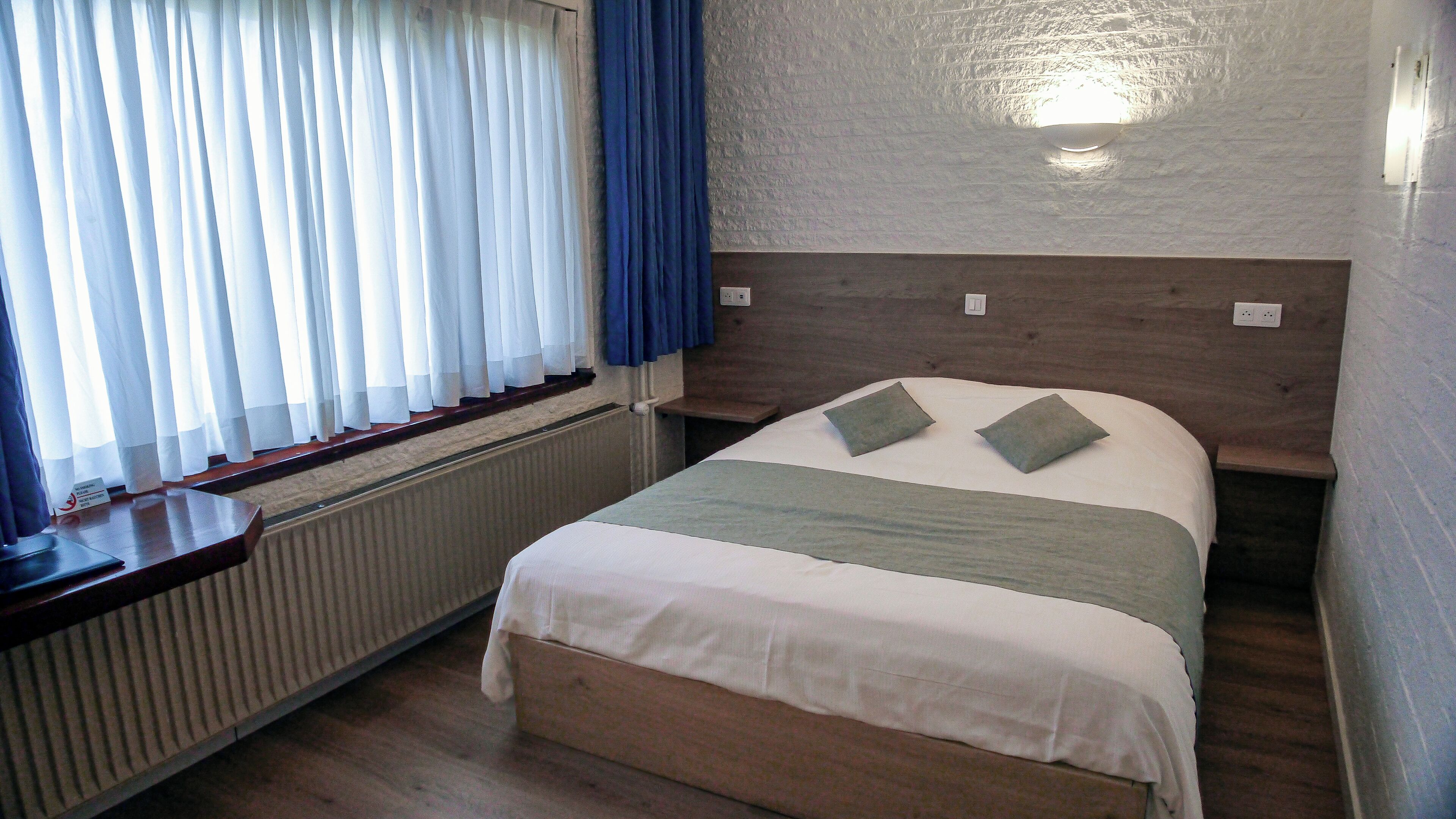 Una cama bien hecha con cabecera de madera, una mesita de noche y una ventana con cortinas.
