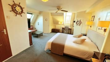Quarto de hotel com cama, escrivaninha, cadeira, ventilador de teto e um leme na parede.