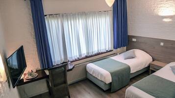 A hotel room with two single beds, a desk with a chair, a television, and a window with curtains.