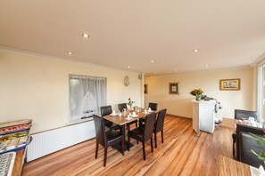 A dining area with a wooden table set for six, surrounded by chairs. There is a white radiator under the window, and a small white cabinet with a vase of flowers on top. - Hotel Marco Polo (Hamburg)