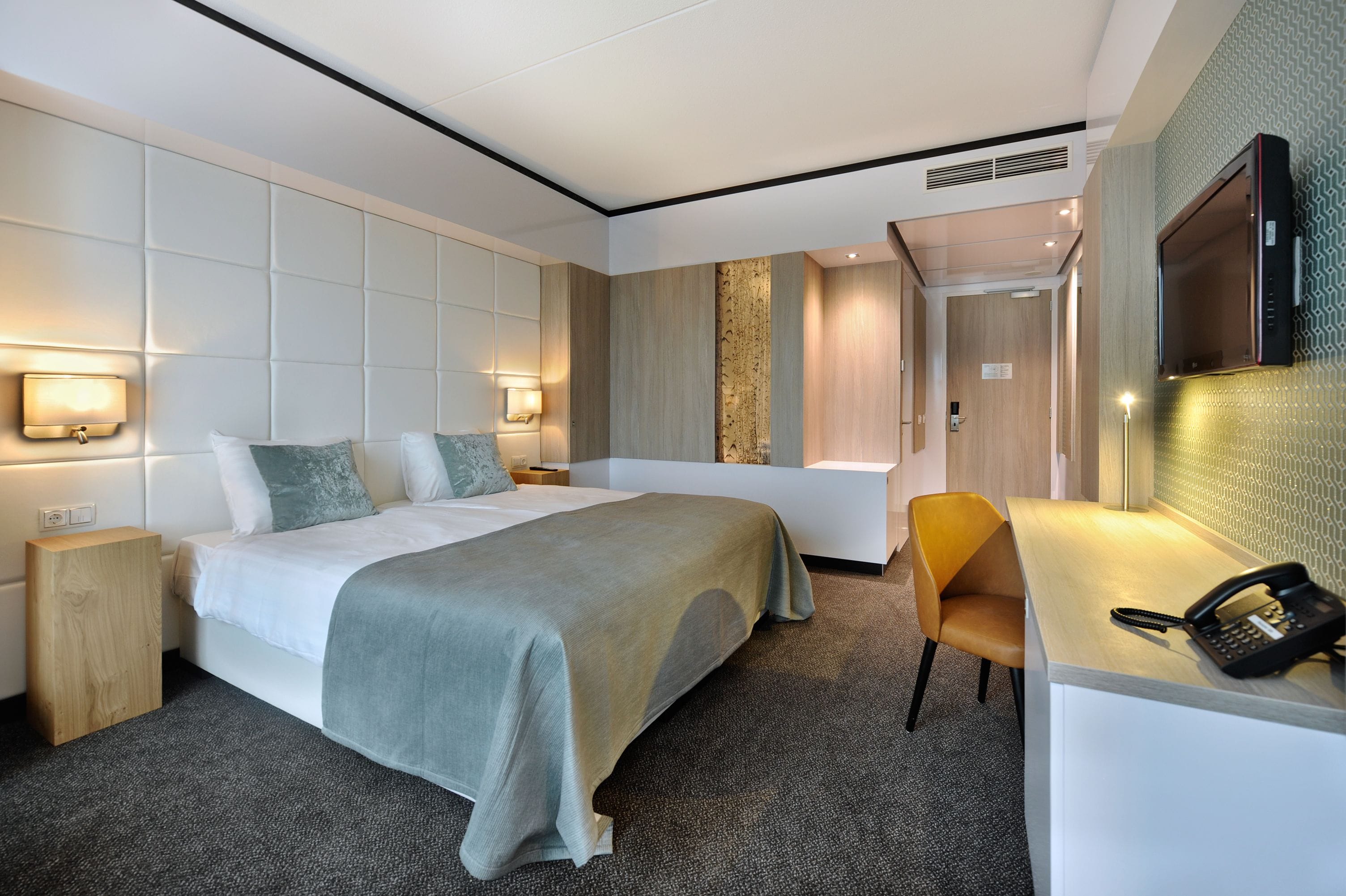 A hotel room with a bed, bedside tables, a desk with a telephone, and a bathroom with a bathtub and shower.