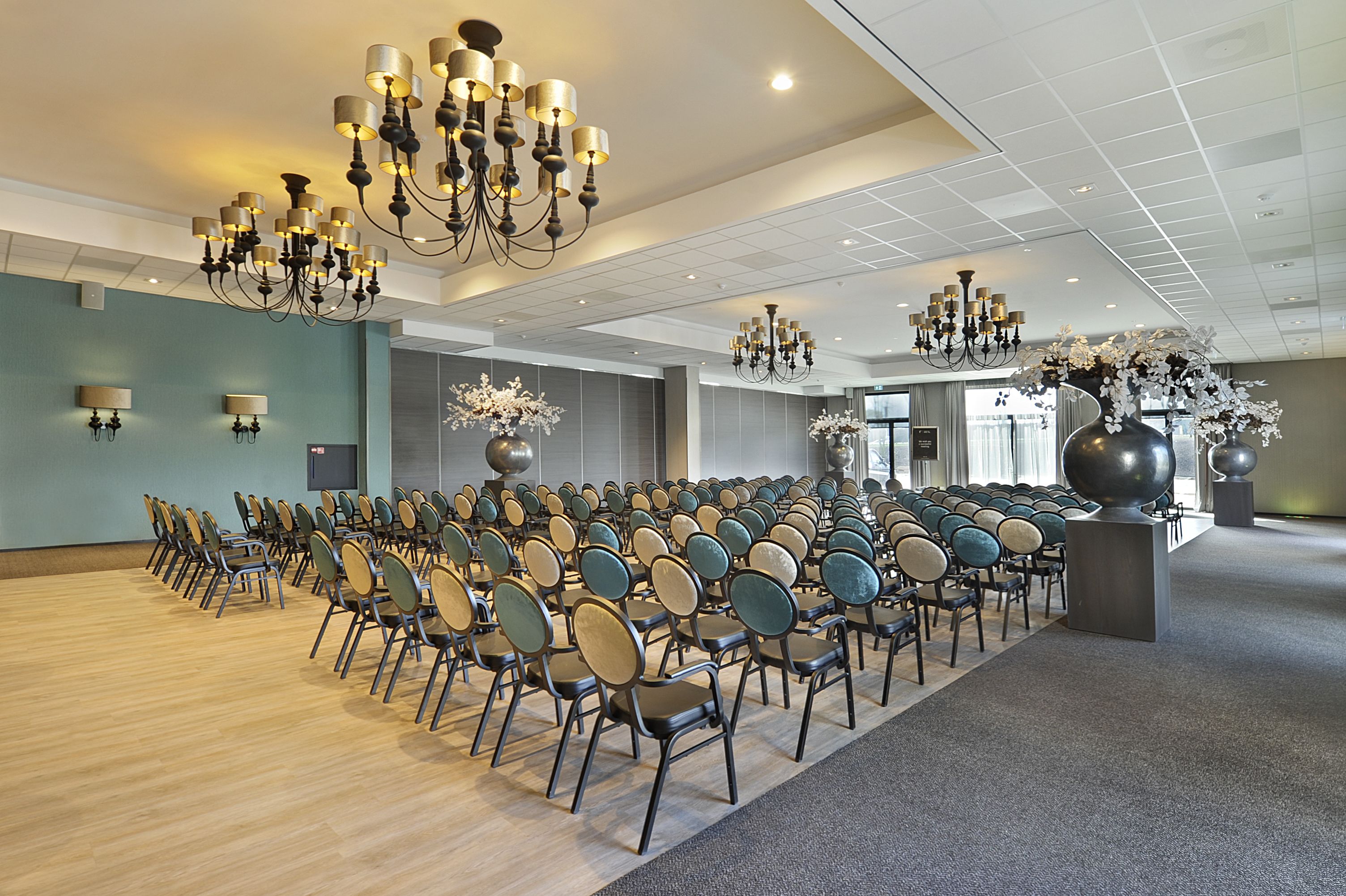 A conference room with rows of chairs, chandeliers, and decorative vases.
