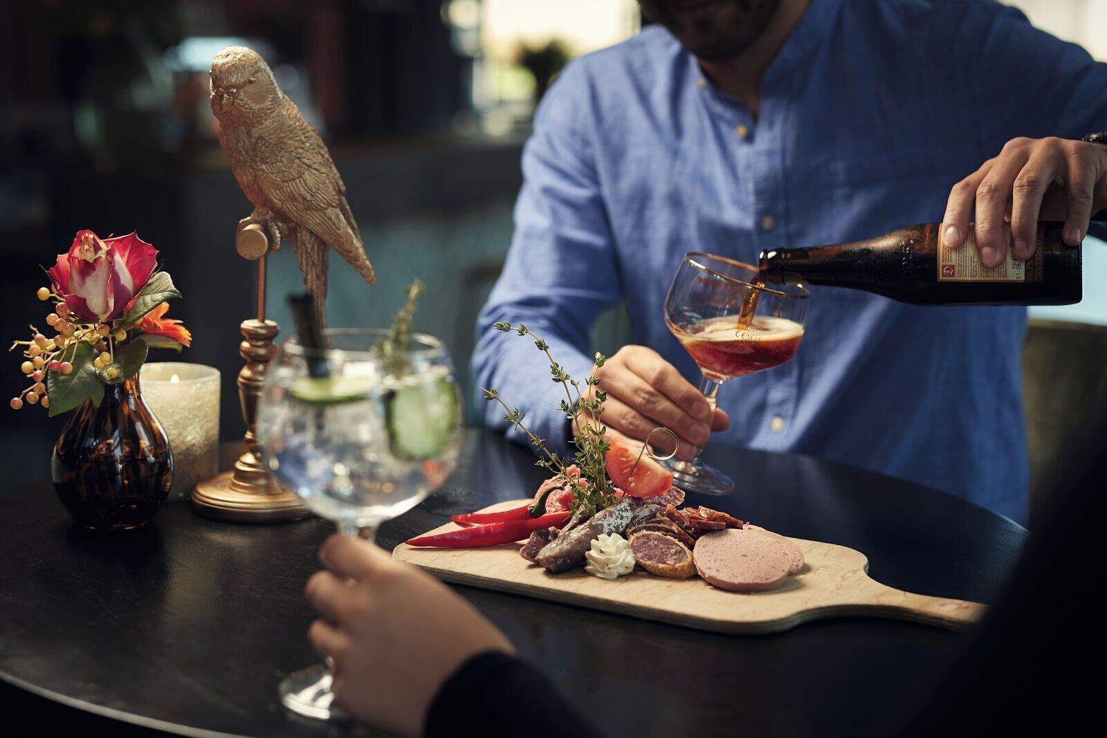 A person pouring a drink into a glass at a table with a variety of food items and a decorative owl.