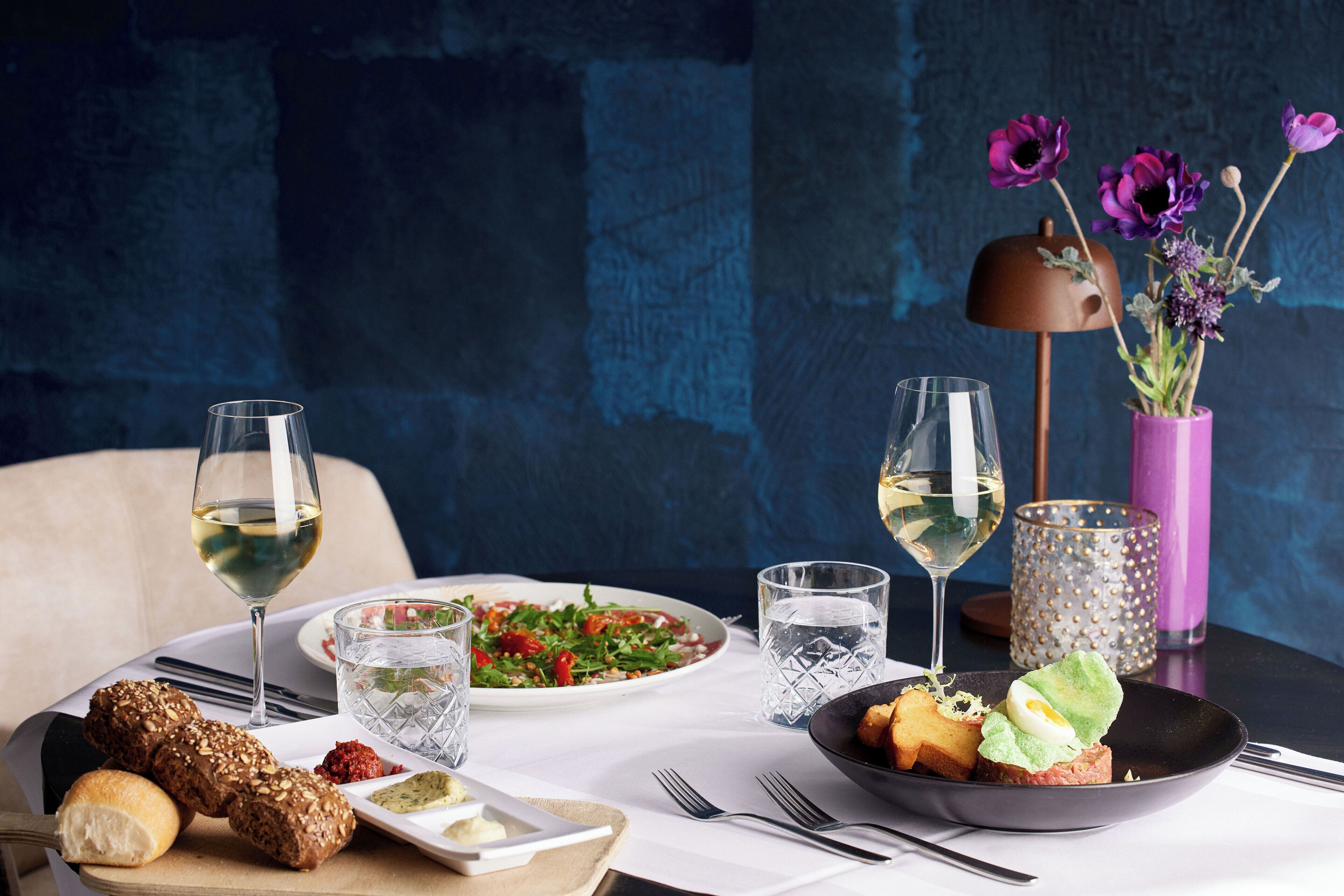 A dining table with a variety of dishes, glasses of wine, and a vase with flowers.