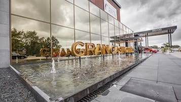 L’entrée d’un hôtel, agrémentée d’un élément décoratif aquatique réfléchissant, et sur laquelle le nom « GRANGRANDE HOTEL » est affiché en caractères bien visibles.