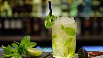 Een cocktail met muntblaadjes, ijsblokjes, een limoenpartje en een cocktailshaker op een bar.