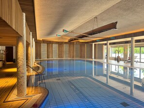 Una amplia piscina interior con agua cristalina y azul, rodeada de paredes y columnas de madera.