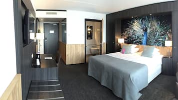 A modern hotel room with a large bed, a desk, a chair, and a peacock mural on the wall.