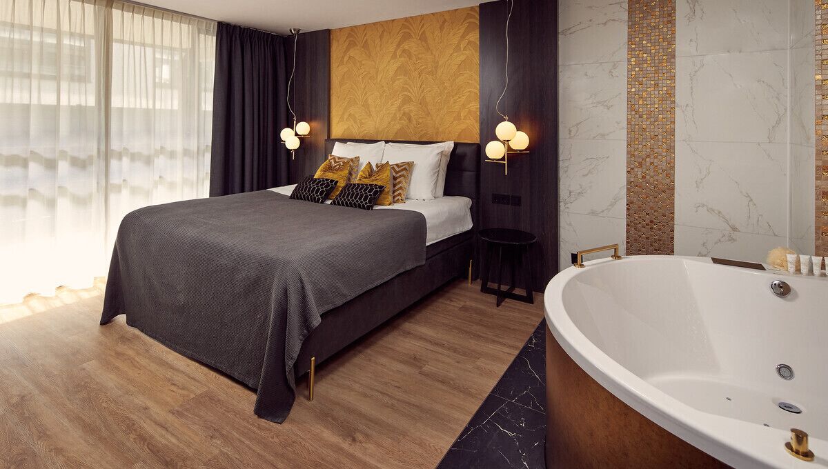 A modern bedroom with a large bed, a sitting area, and a bathtub.