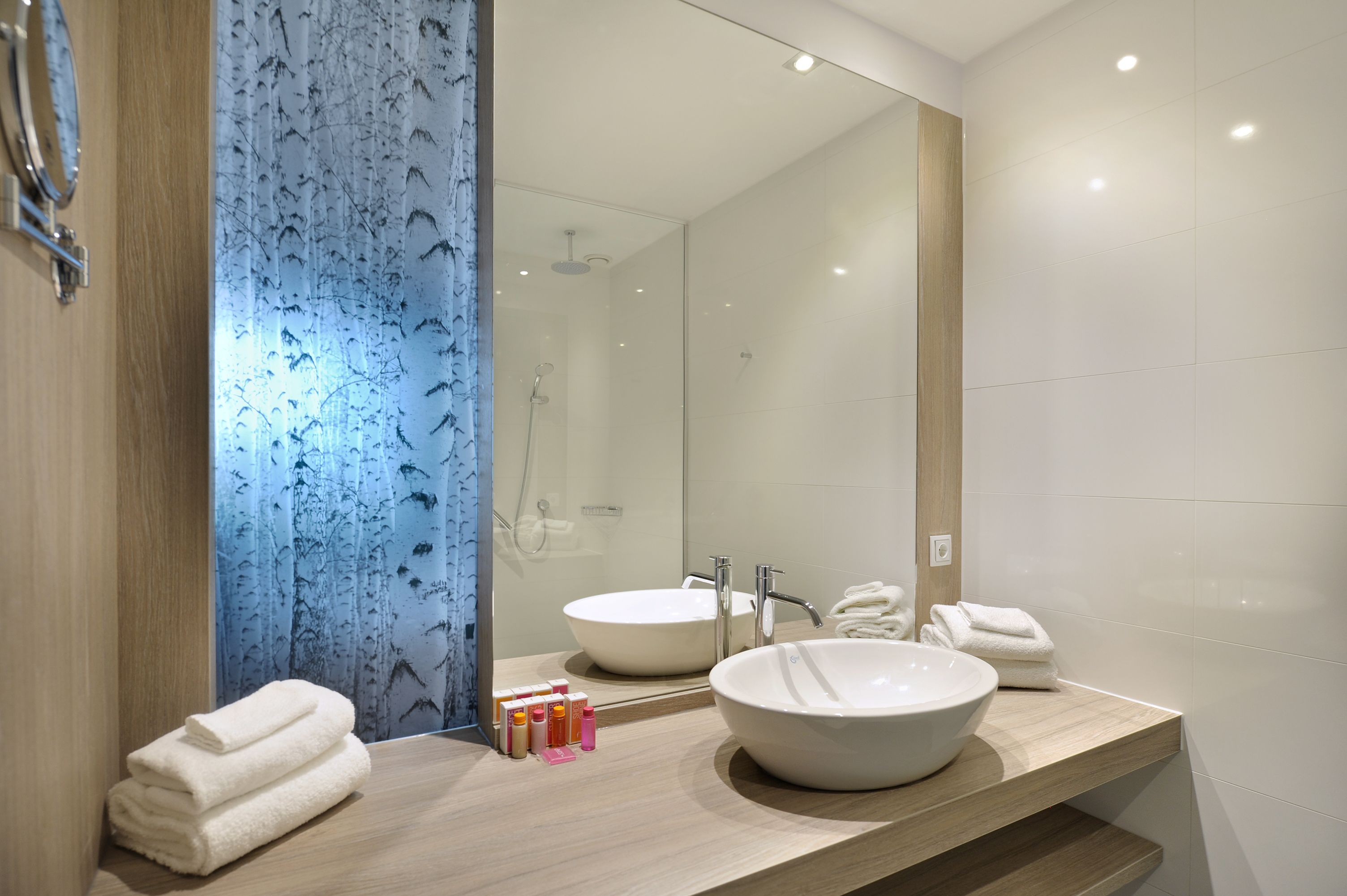 A modern bathroom with a large mirror, two sinks, and a shower.