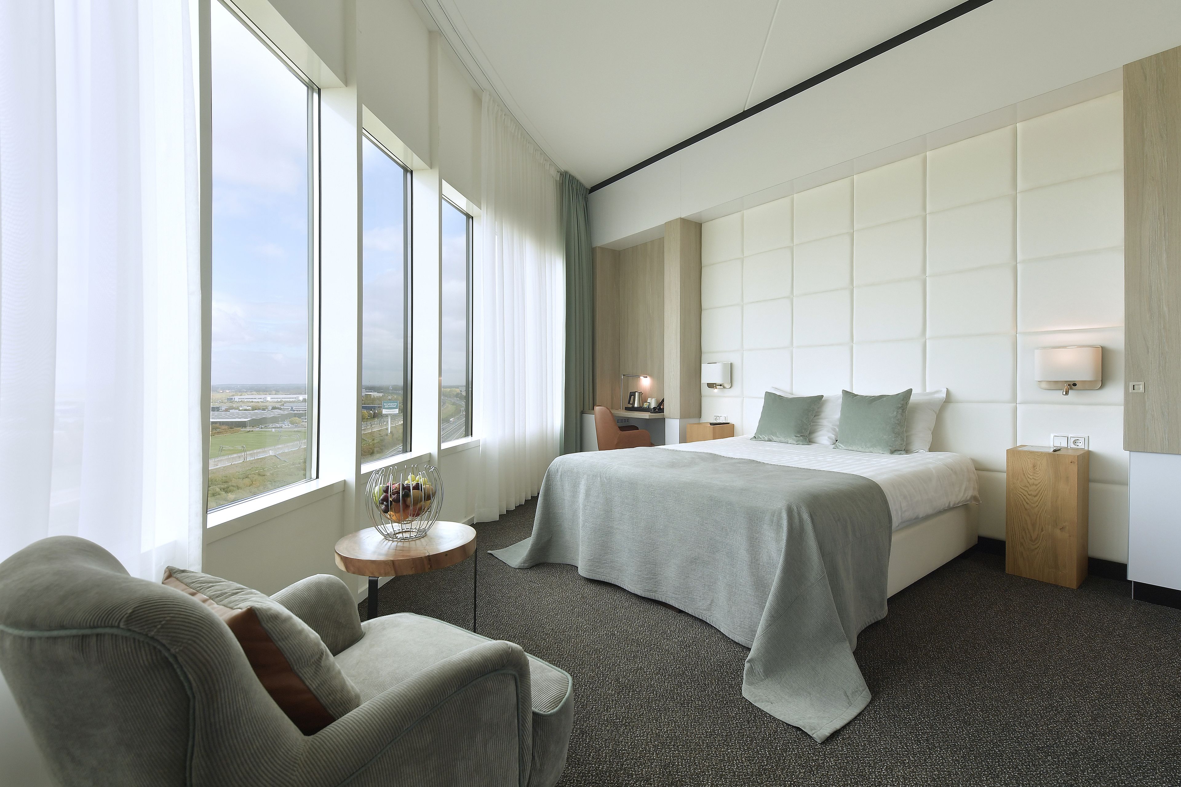 A hotel room with a large bed, a seating area, a small table, and a view of the outdoors.