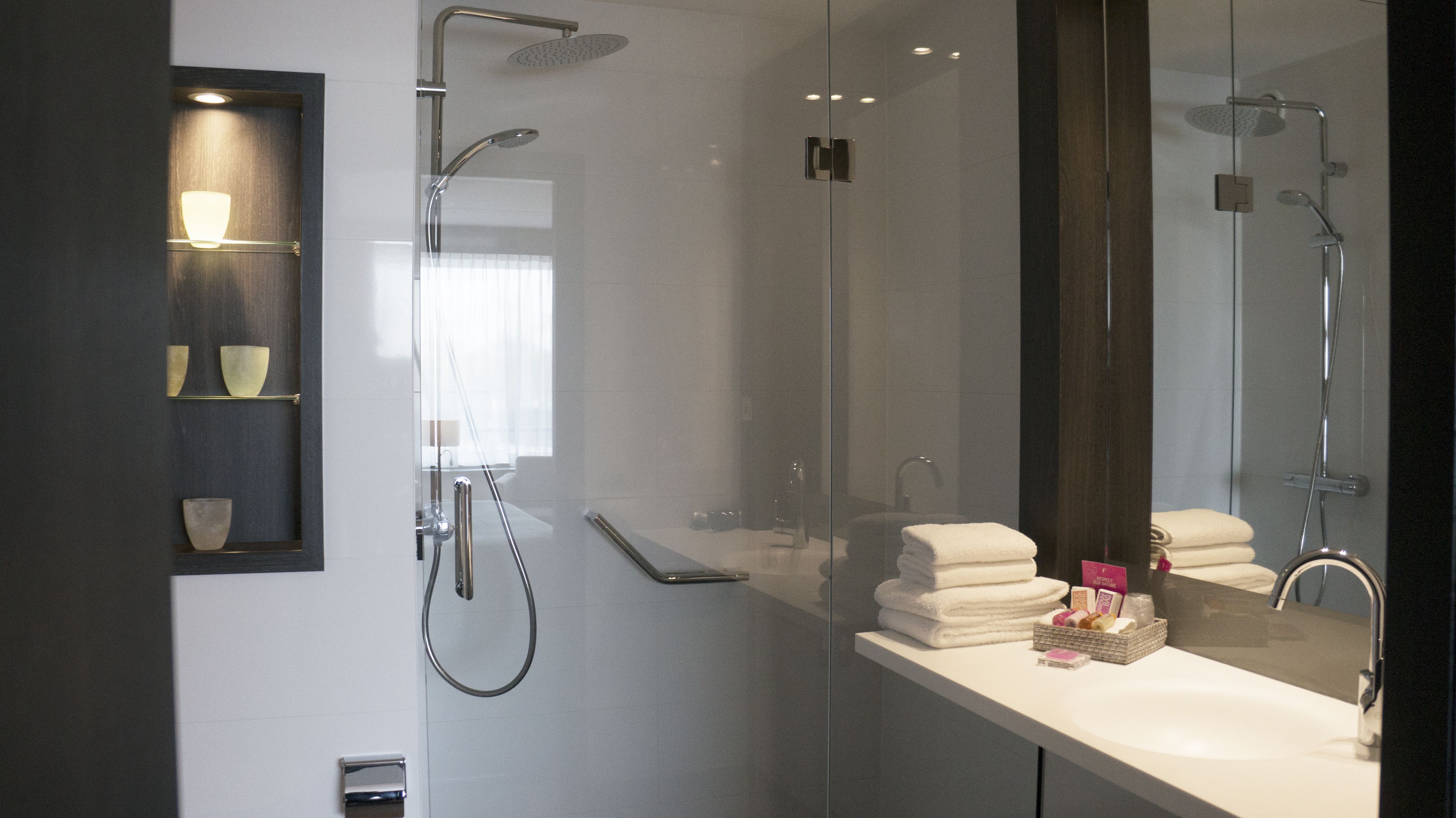 Un baño moderno con cabina de ducha de vidrio, tocador con espejo y perchero.