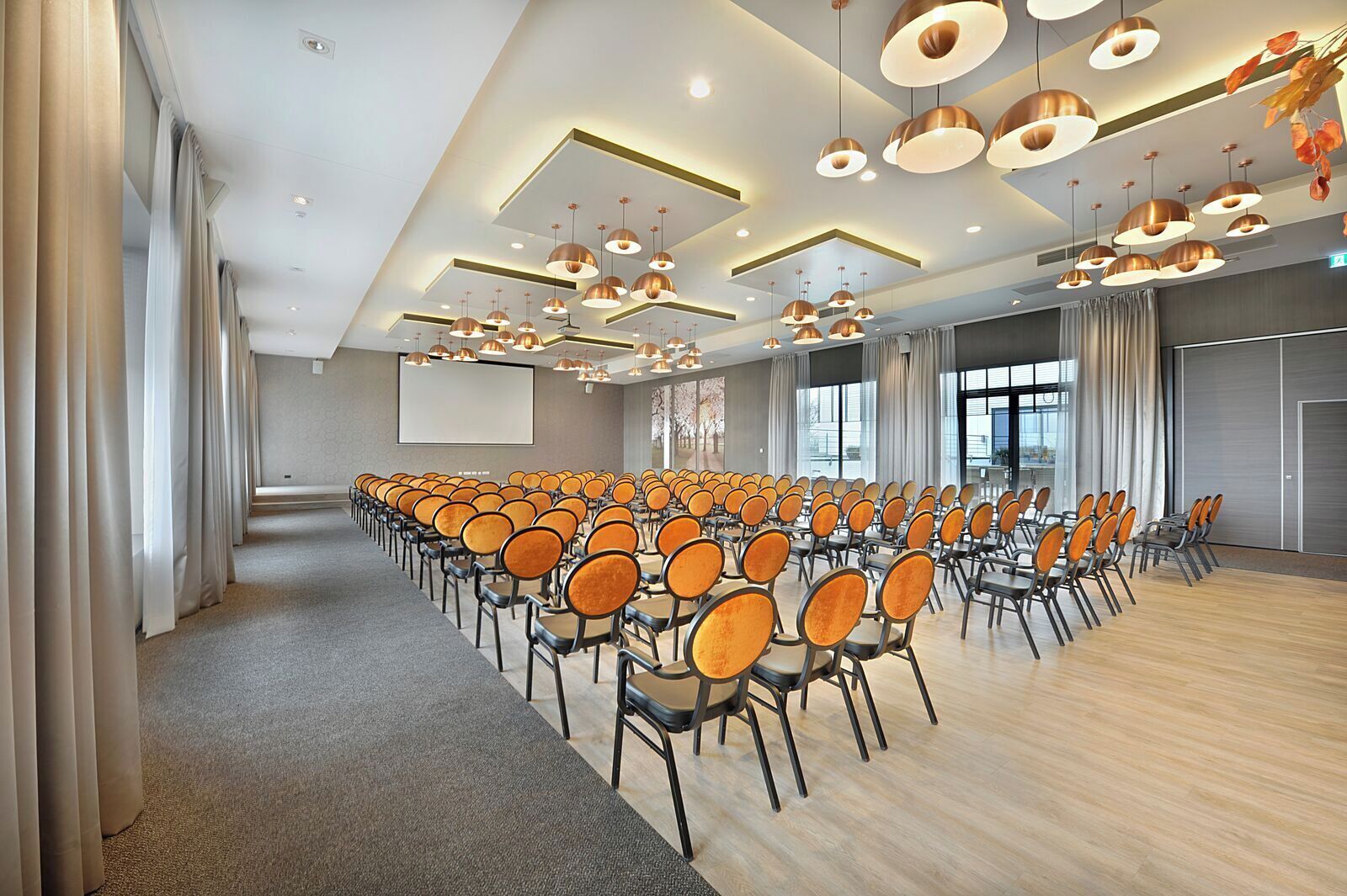 A conference room with rows of chairs, a large screen, and modern pendant lighting.