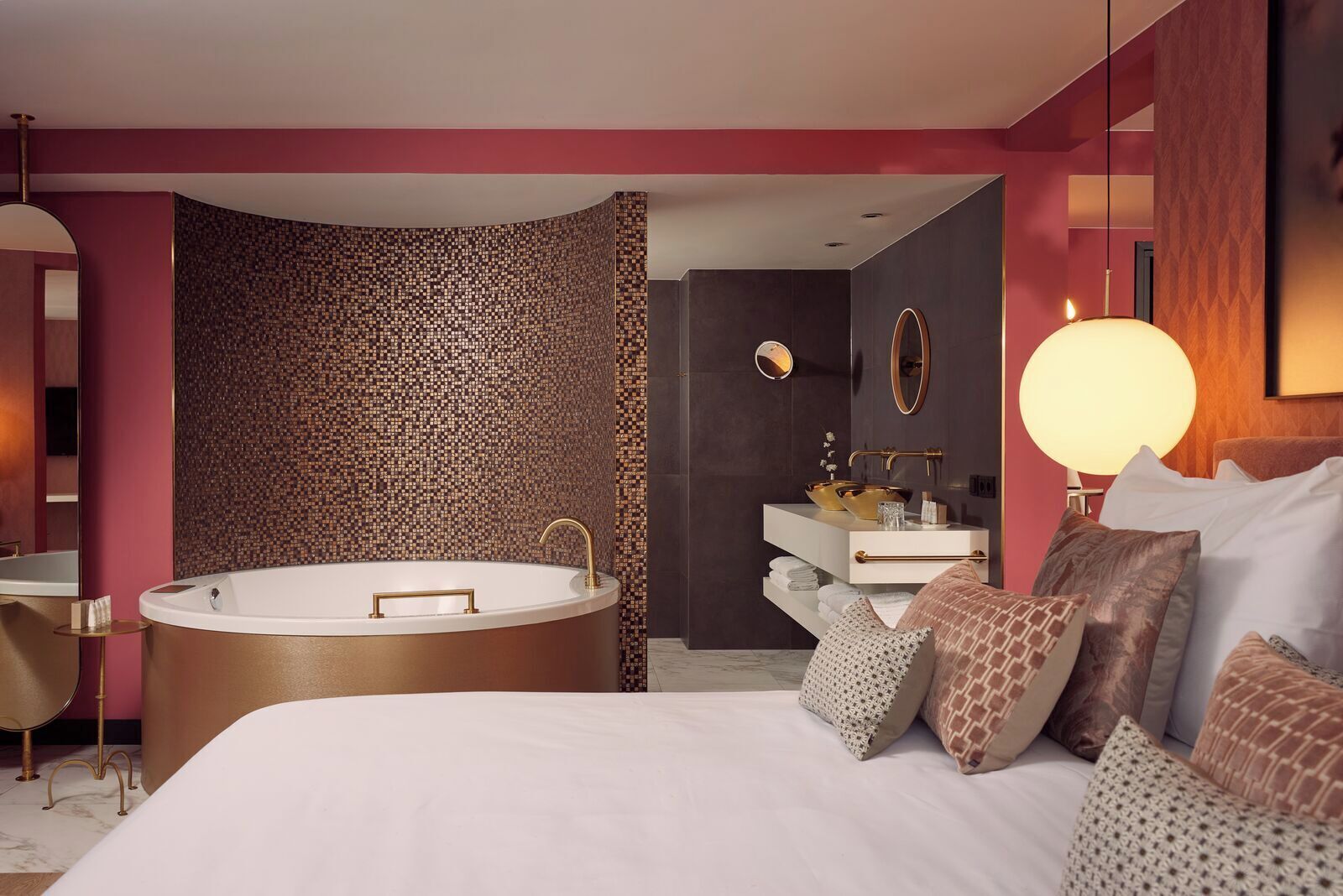 A modern bedroom with a large bed, a freestanding bathtub, a vanity with a mirror, and a round wall-mounted light.