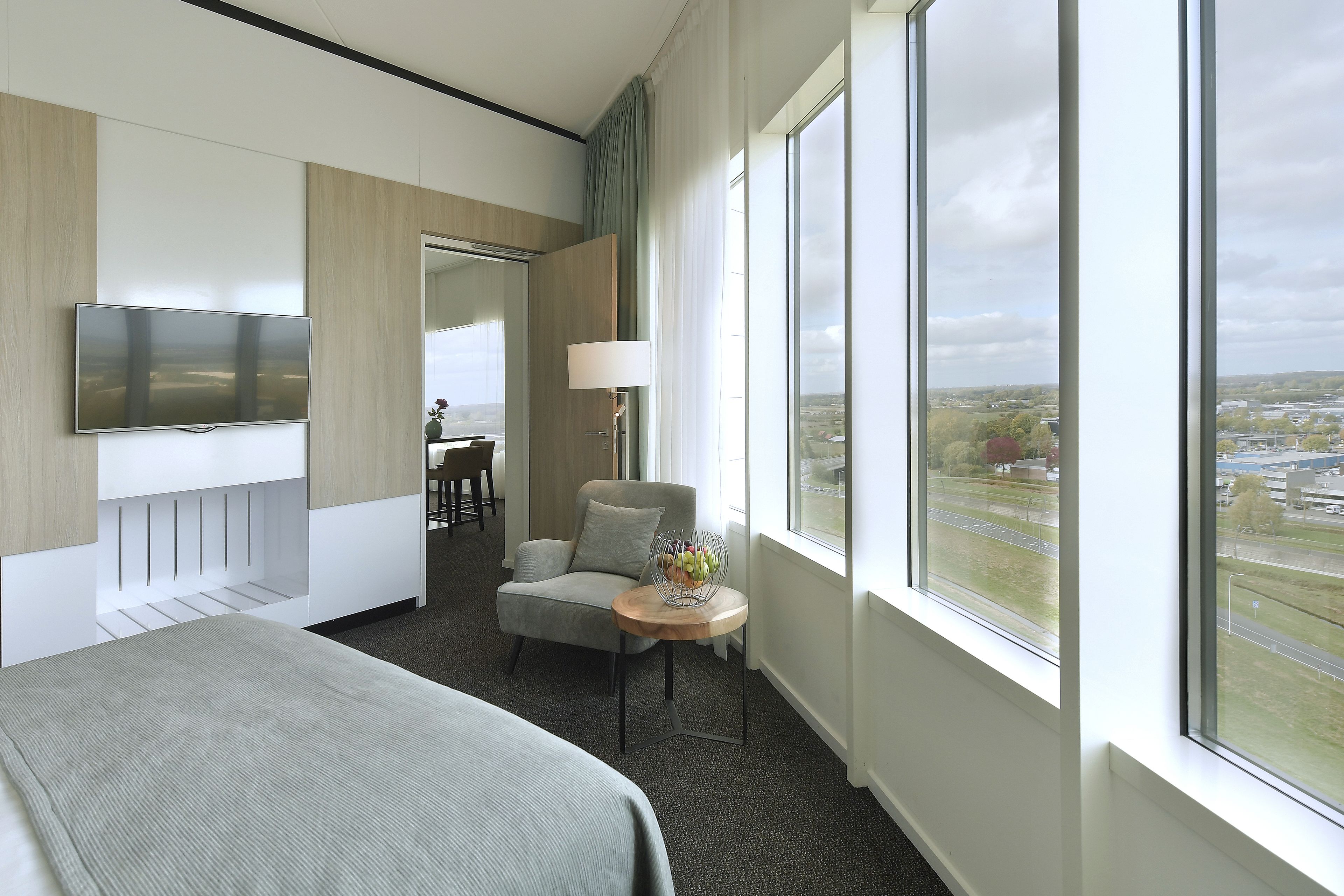 A modern hotel room with a large bed, a TV, a desk, and a chair.