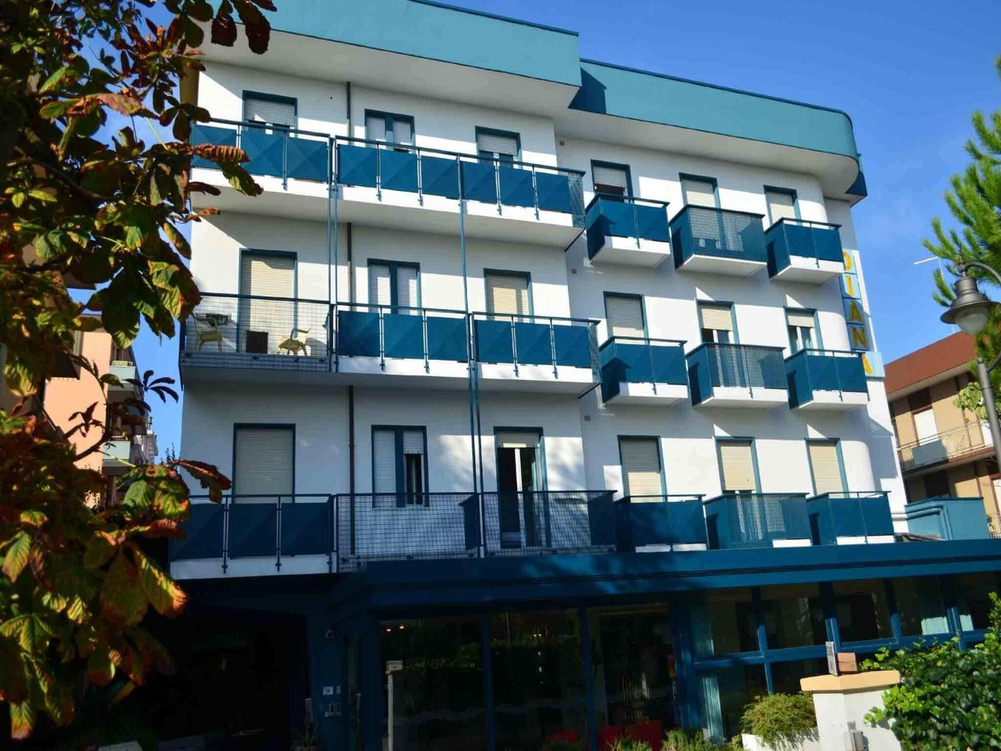 A multi-story hotel with balconies, a glass entrance, and a clear sky.