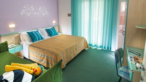 Habitación de hotel con cama, escritorio con silla, sofá verde, un peluche y una ventana con cortinas.